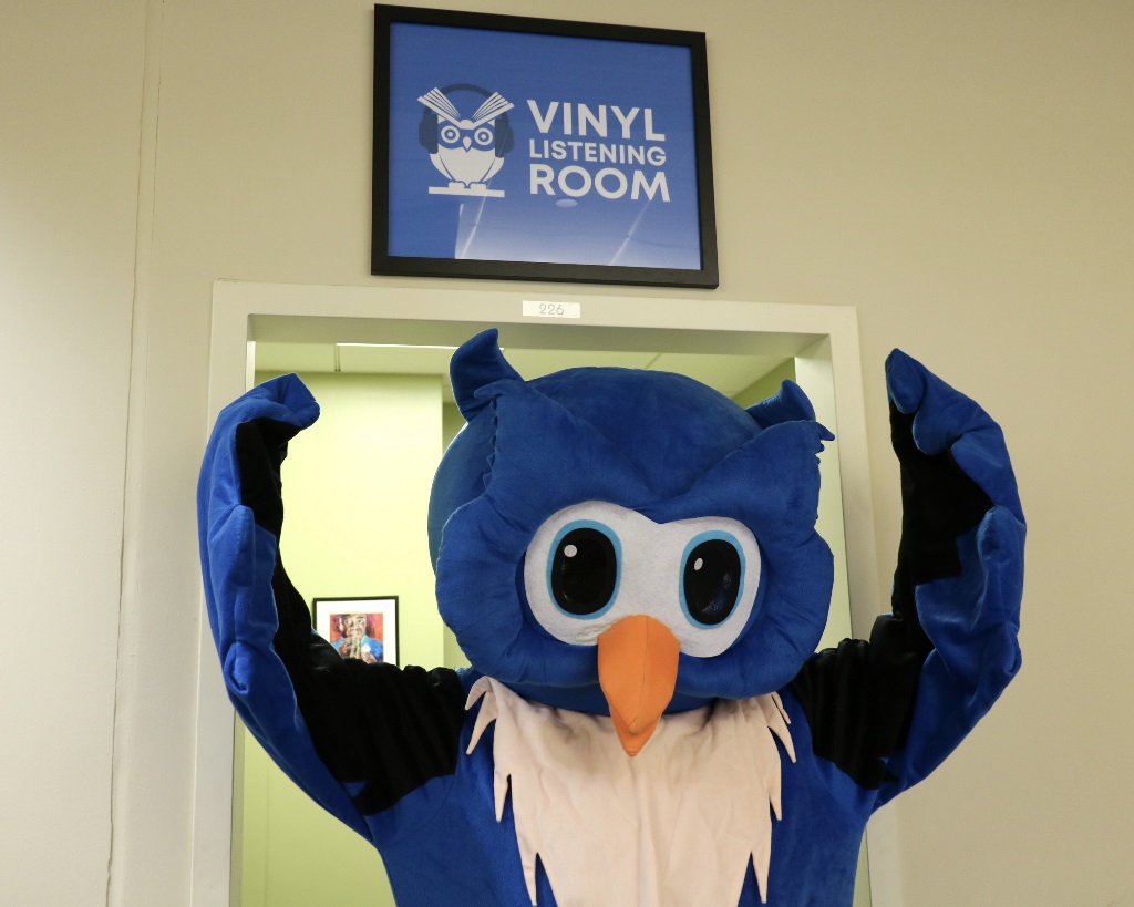 Vinyl Listening Room Sign WFPL mascot, Whooo, points at Vinyl Listening Room sign