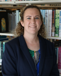 Rachel Nicholas-Kahalley Professional headshot of Rachel Nicholas-Kahalley smiling and looking directly at the camera. She is wearing business attire and is photographed in front of a bookshelf filled with books