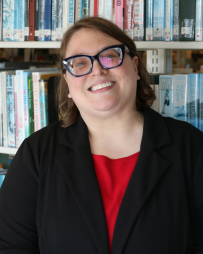 Professional headshot of Vanessa Trask smiling and looking directly at the camera. She is wearing business attire and is photographed in front of a bookshelf filled with books