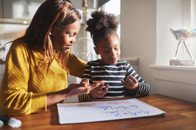 Caretaker and child doing homework together at a kitchen table.